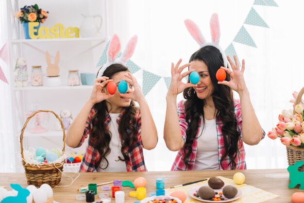 Zakończenie córka i jej matka trzyma czerwonych i błękitnych Easter jajka w ręce patrzeje each inny