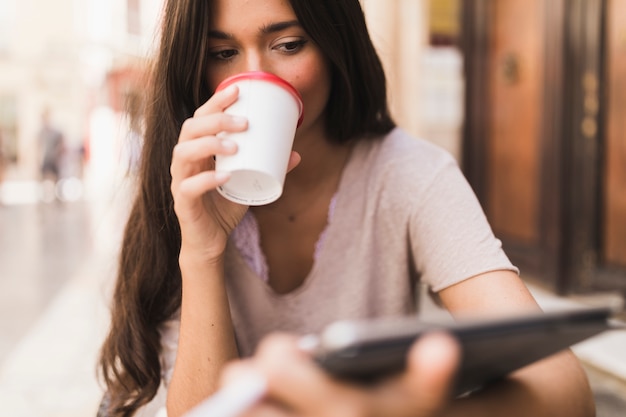 Zakończenie dziewczyna trzyma cyfrową pastylkę pije takeaway kawę