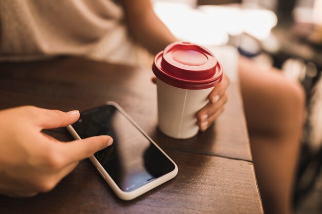 Zakończenie dziewczyna wyszukuje na mądrze telefonie trzyma rozporządzalną filiżankę