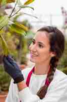 Bezpłatne zdjęcie zakończenie kobieta jest ubranym ogrodnictwo odzieżowy i dotyka rośliny w szklarni