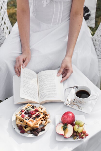 Zakończenie kobieta obraca strony książka z śniadaniem i kawą na stole
