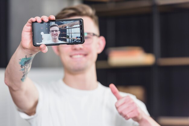 Zakończenie mężczyzna bierze selfie na telefonie komórkowym pokazuje kciuk up podpisuje