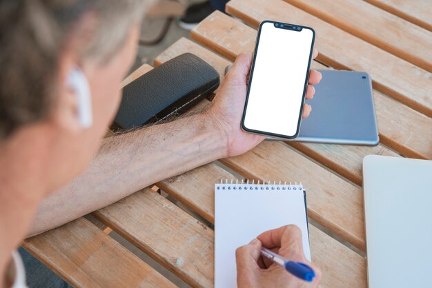 Zakończenie mężczyzna mienia smartphone writing na ślimakowatym notepad z piórem