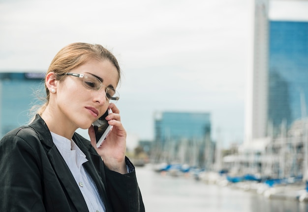 Zakończenie młody bizneswoman jest ubranym eyeglasses opowiada na telefonie komórkowym przy outdoors