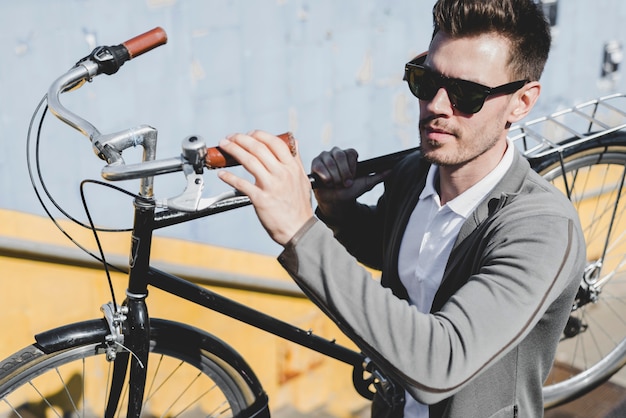 Zakończenie młody człowiek jest ubranym okulary przeciwsłonecznych niesie bicykl na jego ramieniu