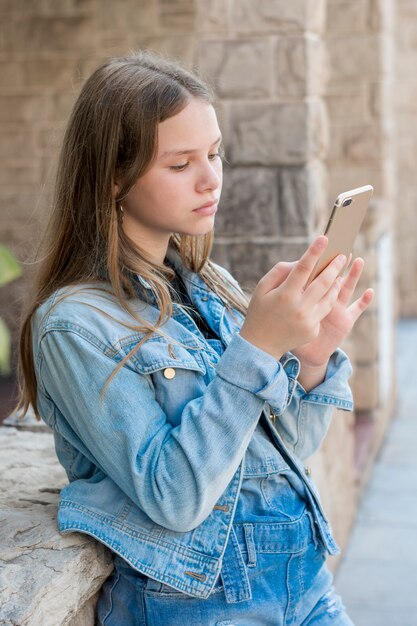 Zakończenie nastoletnia dziewczyna w drelichu używać mądrze telefon przy outdoors