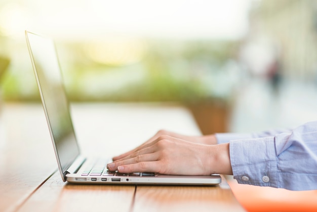Bezpłatne zdjęcie zakończenie osoby ręka pracuje na laptopie nad drewnianym biurkiem