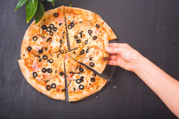 Zakończenie ręki mienia plasterek pizza na ciemnym tle