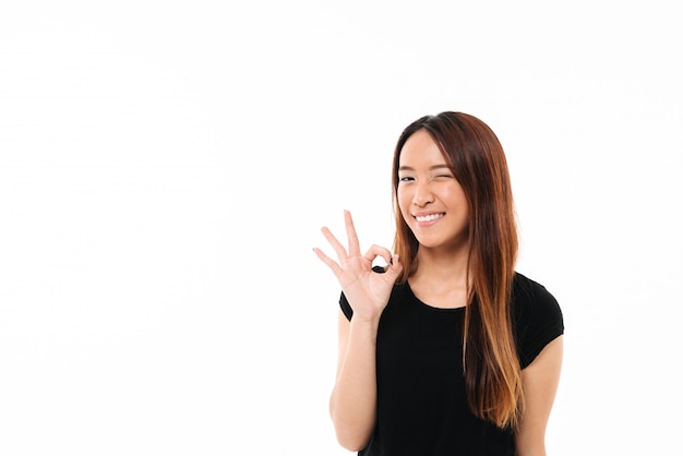 Zakończenie rozochocona ładna azjatykcia kobieta mruga i pokazuje OK gest
