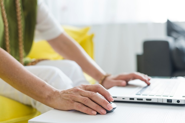 Zakończenie starszej kobiety ręka używać myszy i laptopu
