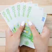 Bezpłatne zdjęcie zakończenie trzyma sto euro banknotów na drewnianym stole ludzka ręka