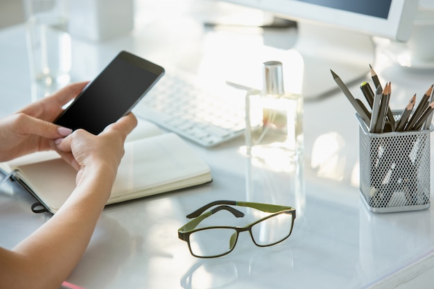 Zakończenie żeńskie Ręki Używać Telefon Podczas Gdy Pracujący Na Komputerze Przy Nowożytnym Biurowym Wnętrzem