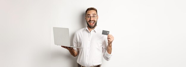 Zakupy online przystojny mężczyzna pokazując kartę kredytową i używając laptopa, aby zamówić w internecie, stojąc nad