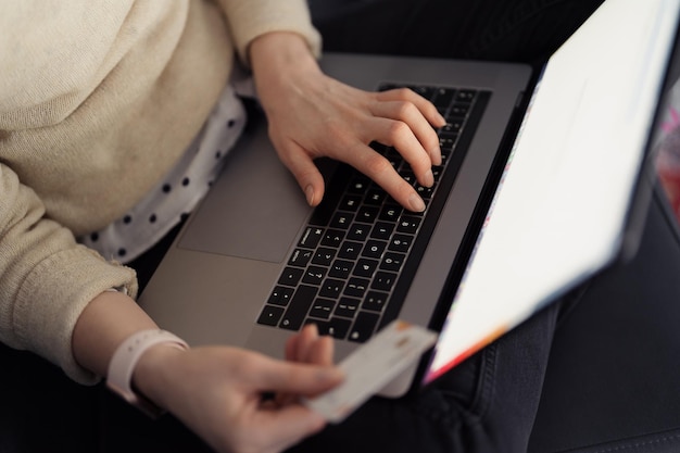 Zakupy online za pomocą karty i laptopa Kobieta używająca technologii do robienia zakupów, siedząc na sofie w pomieszczeniu
