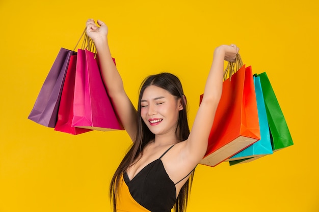 Zakupy piękna kobieta trzyma kolorową papierową torbę na kolorze żółtym.
