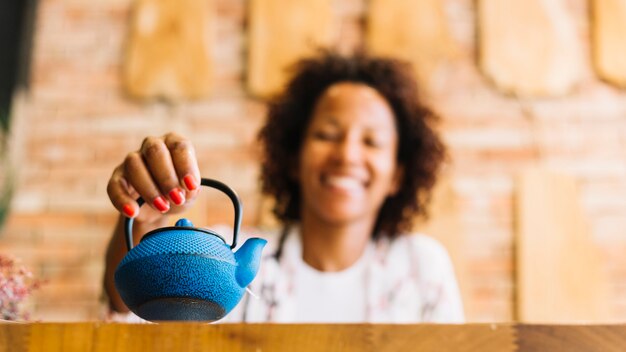 Zamazana młoda kobieta trzyma błękitnego czajnika w ręce