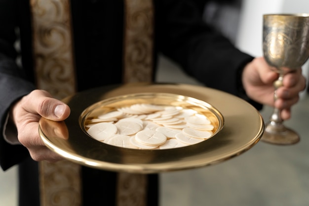 Bezpłatne zdjęcie zamknij się ksiądz trzymający talerz i eucharystię