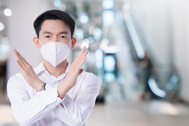 Zamknij się młody azjatycki biznesmen płci męskiej noszący maskę przeciw zanieczyszczeniom z gestem, krzyżem, aby powiedzieć, że nie ma białego tła