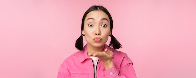 Zamknij Się Portret Pięknej Głupiej Azjatyckiej Dziewczyny Wysyłającej Powietrze Pocałunek Mwah W Kamerę, Która Wieje Stojąc Na Różowym Tle