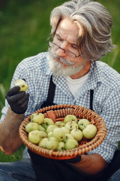 Bezpłatne zdjęcie zamknij się stary rolnik posiadający kosz warzyw. mężczyzna stoi w ogrodzie. senior w czarnym fartuchu.