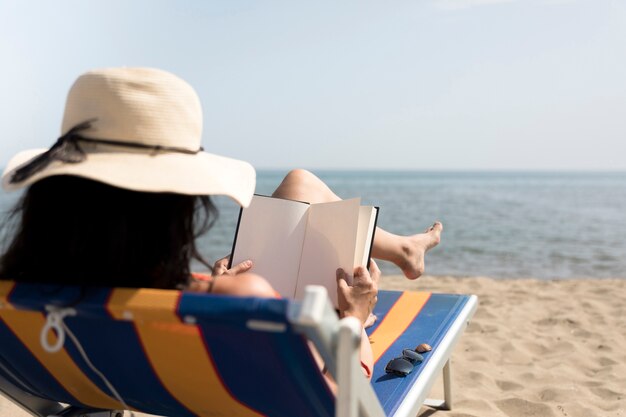 Zamknij się widok z tyłu kobieta na krześle plaży czytania