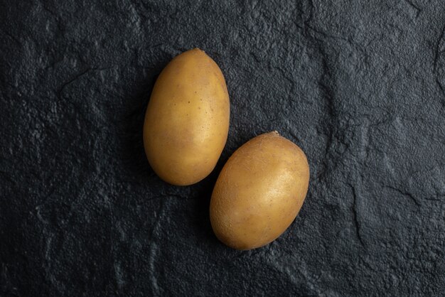 Zamknij się zdjęcie dwóch świeżych ziemniaków na czarnym tle.