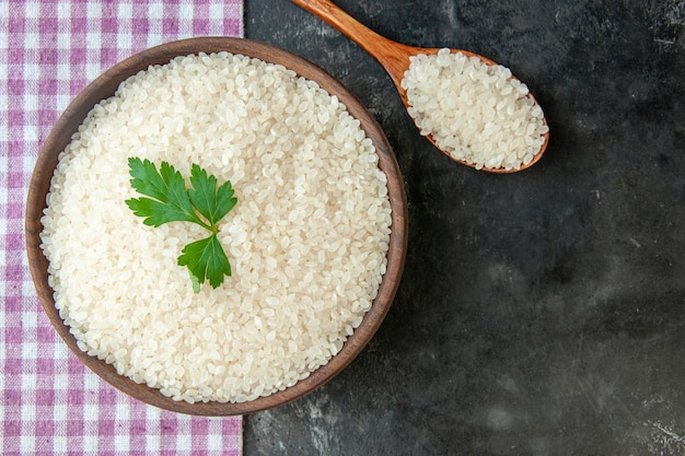 Zamknij widok idealnego okrągłego ryżu w brązowej misce z zielonym na fioletowym ręczniku w paski i drewnianą łyżką na ciemnym tle
