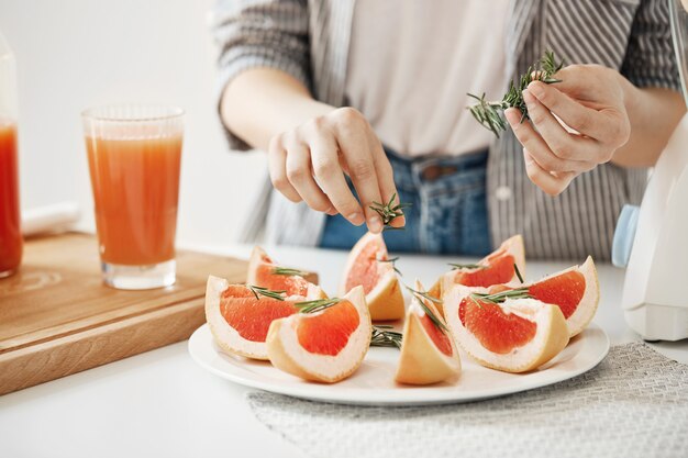 Zamyka up dziewczyna dekoruje talerza z pokrojonym grapefruitowym i rozmarynowym. Koncepcja żywienia fitness. Skopiuj miejsce