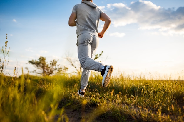 Zamyka up sportive mężczyzna jogging w polu przy wschodem słońca.