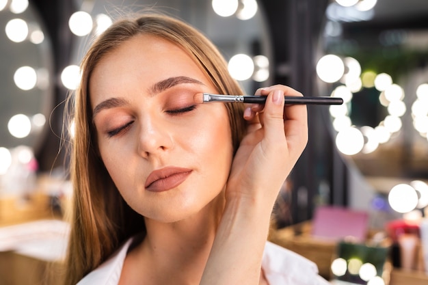 Zamyka w górę makijażu artysty stosuje eyeshadow na kobiecie z muśnięciem
