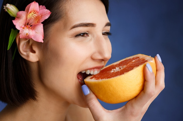 Zamyka w górę portreta czułego młodej kobiety mienia rżnięta pomarańcze nad błękit ścianą