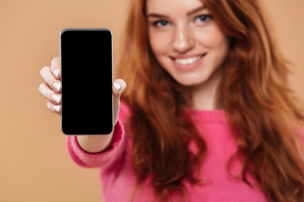 Zamyka w górę portreta szczęśliwa atrakcyjna rudzielec dziewczyna pokazuje smartphone
