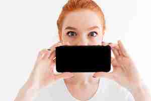 Bezpłatne zdjęcie zamyka w górę wizerunku imbirowa kobieta pokazuje pustego smartphone ekran i zakrywa jej usta