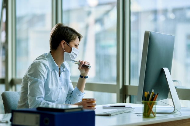 Zamyślona bizneswoman z maską siedzi przy biurku i myśli o czymś