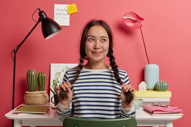 Zamyślona Hipsterka Myśli O Pomysłach Na Pracę Badawczą, Siedzi W Przestrzeni Coworkingowej Naprzeciw Biurka Z Notatnikami, Teczką I Książkami Dookoła