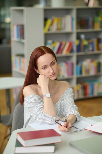 Zamyślona kobieta siedzi przy stole w bibliotece