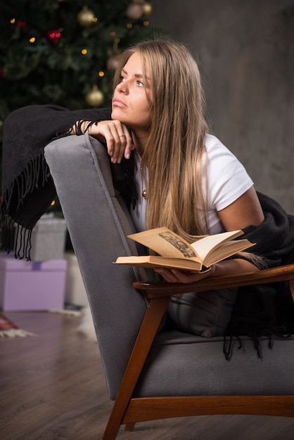 Zamyślona młoda kobieta w czarnym kocu siedzi z książką
