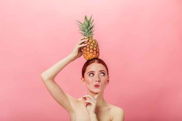 Zamyślona naga kobieta trzyma ananas. Imbir kaukaski dziewczyna z egzotycznymi owocami i odwracając wzrok.