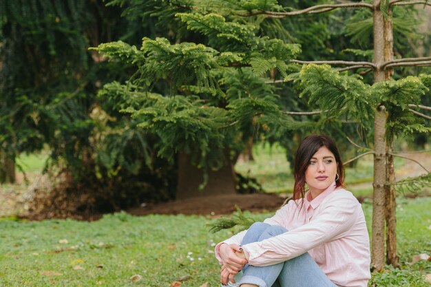 Zamyślony kobieta siedzi na trawniku w pobliżu drzew