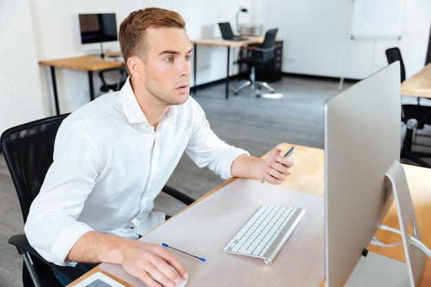 Zamyślony młody biznesmen siedzi w biurze i pracuje z komputerem