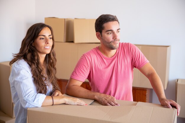 Zamyślony młody mężczyzna i kobieta stoją wśród pudeł w mieszkaniu, odwracając wzrok
