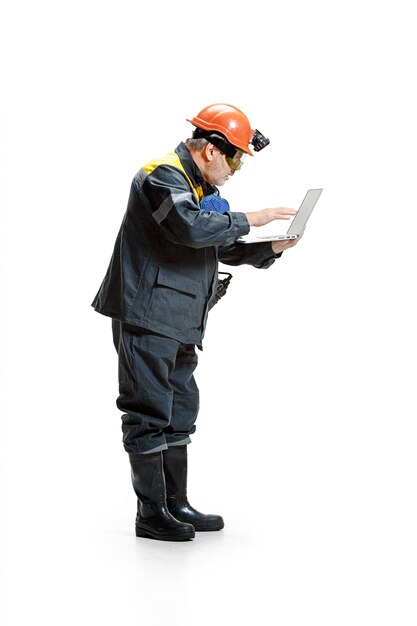 zamyślony starszy brodaty mężczyzna górnik stojący w widoku profilu w aparacie z laptopem na białym tle