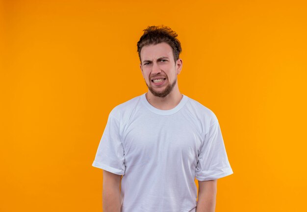 Zaniepokojony młody człowiek ubrany w białą koszulkę na odosobnionej pomarańczowej ścianie