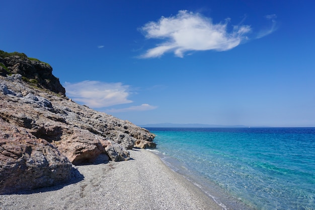 Zapierające dech w piersiach ujęcie przedstawiające spotkanie błękitnego morza ze słoneczną kamienistą plażą pod błękitnym niebem
