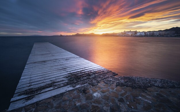 Zapierający dech w piersiach widok na pejzaż morski z drewnianym molo o malowniczym dramatycznym zachodzie słońca