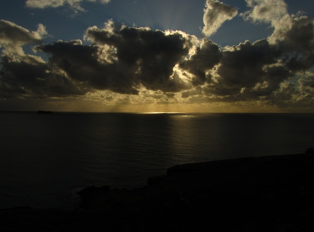 Zapierający dech w piersiach zachód słońca nad oceanem z wysepką Filfla na Malcie w pochmurny dzień