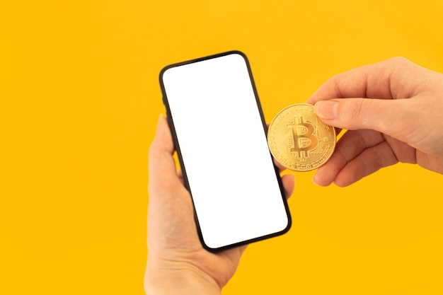 Zapłać makieta bitcoin z pustym białym ekranem, żółtym tłem z telefonem komórkowym i monetą bitcoin w ręku kobiety, skopiuj zdjęcie miejsca