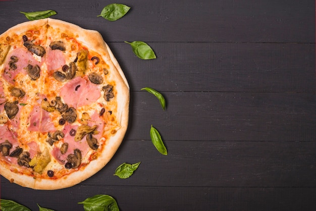 Zasięrzutny widok domowej roboty pizza dekorował z basilem opuszcza na drewnianej desce