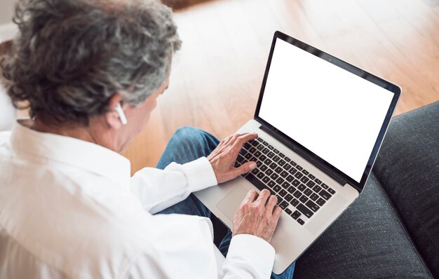 Zasięrzutny widok jest ubranym bluetooth słuchawkę używać laptop starszy mężczyzna