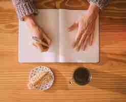 Bezpłatne zdjęcie zasięrzutny widok kobiety writing na pustym białym notatniku z piórem i śniadaniem na stole